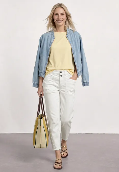 Frau im lässigen Outfit: hellblaues Jackett, gelbes Shirt, weiße Hose, Sandalen und gelbe Tasche.
