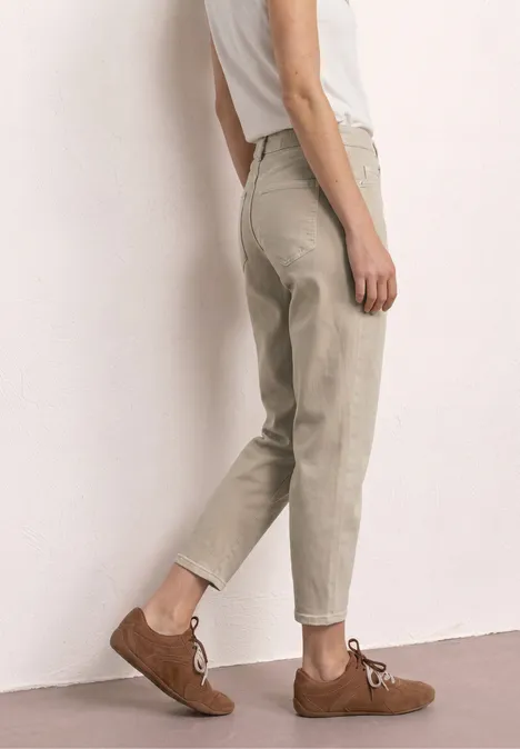 Unterkörper einer Person mit beigen, lässigen Hosen und braunen Schnürschuhen vor neutralem Hintergrund.