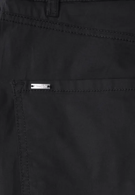 Detailaufnahme einer schwarzen Hose mit silbernem Markenlogo auf Gesäßtasche.