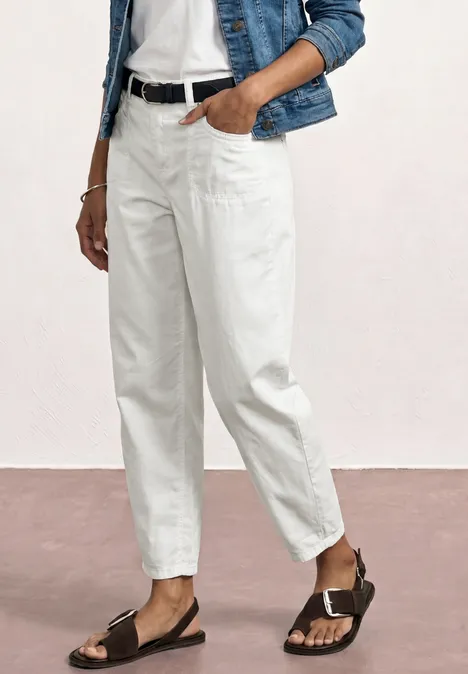 Weiße Bundfaltenhose mit schwarzem Gürtel, Jeansjacke, weißem Top und schwarzen Sandalen.