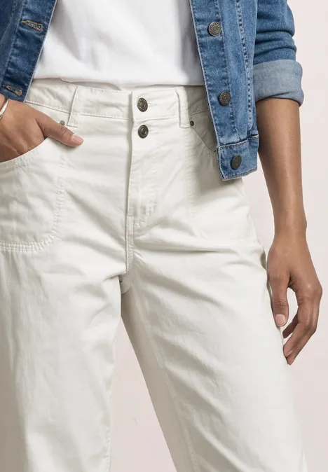 Person trägt helle Jeans mit hoher Taille und Doppelknopf, kombiniert mit weißem Shirt und Jeansjacke.