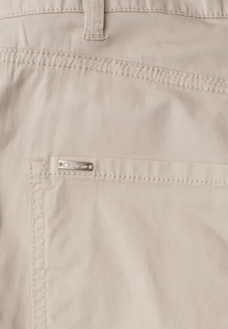 Close-up einer hellbeigen Hose mit aufgesetzter Tasche und kleinem Metalllogo.