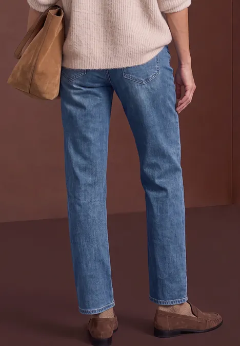 Mid Waist Straight Leg Jeans im Casual Fit Dark blue washed Person von hinten, trägt blaue Jeans, hellen Pullover, braune Tasche und Schuhe.