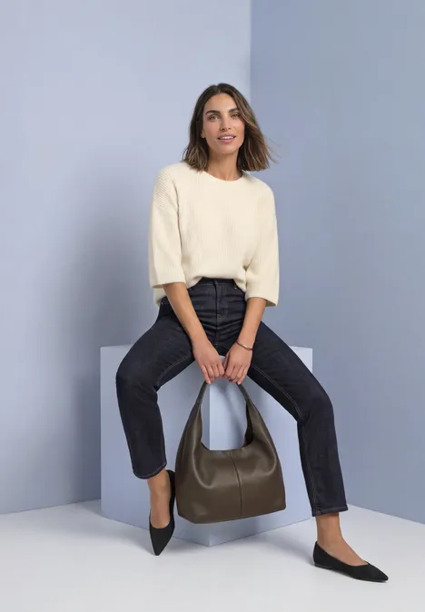 Mid Waist Straight Leg Jeans im Casual Fit Rinse Washed Frau im hellen Pullover und dunklen Hosen sitzt auf Block und hält eine olivgrüne Handtasche.