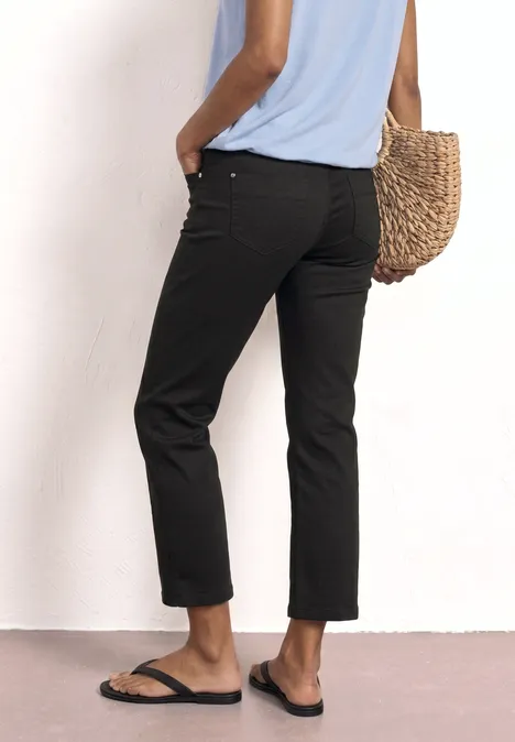 Personne vue de dos porte un pantalon 7/8 noir, t-shirt bleu, sac en paille et sandales noires.