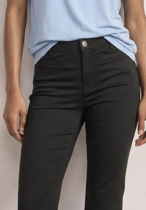 Gros plan d’une personne portant un jean noir taille haute et un haut bleu clair.
