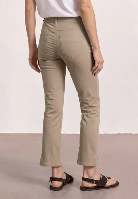Femme de dos portant un pantalon beige évasé 7/8 et des sandales noires sur fond neutre.