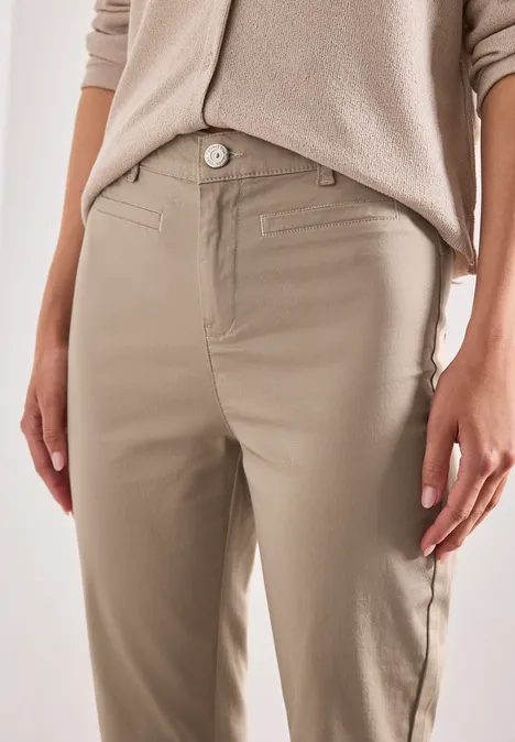 Gros plan d'une personne portant un pantalon chino beige avec poches latérales et pull clair.
