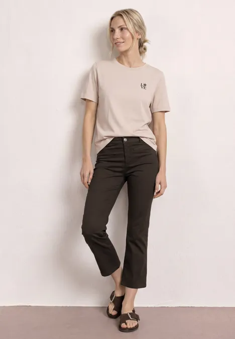 Vrouw in beige T-shirt, zwarte 7/8-broek en sandalen voor een neutrale achtergrond.