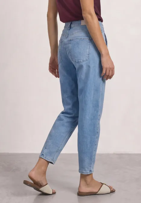 High Waist Barrel Leg Jeans im Loose Fit Light Blue Wash Frau trägt hochgeschnittene, hellblaue Jeans mit schmal zulaufendem Bein und cremefarbene Pantoletten.