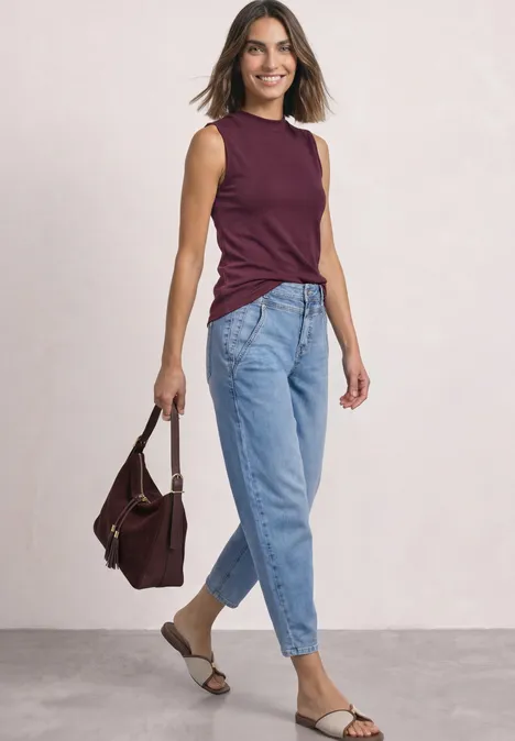 High Waist Barrel Leg Jeans im Loose Fit Light Blue Wash Frau in Jeans, ärmellosem dunkelrotem Top, Sandalen und Tasche, die lächelnd posiert.