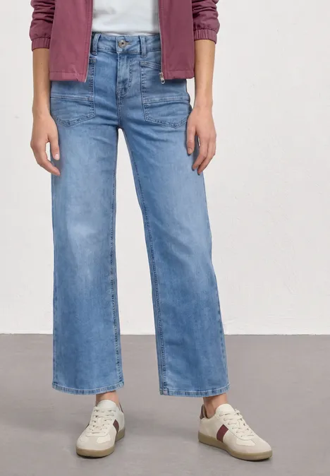 Person trägt leichte, gerade geschnittene Jeans im Cropped-Stil und weiße Sneaker.