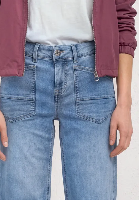Person trägt helle Jeans, weißes Shirt und rote Jacke, nur Oberkörper und Hände sichtbar.