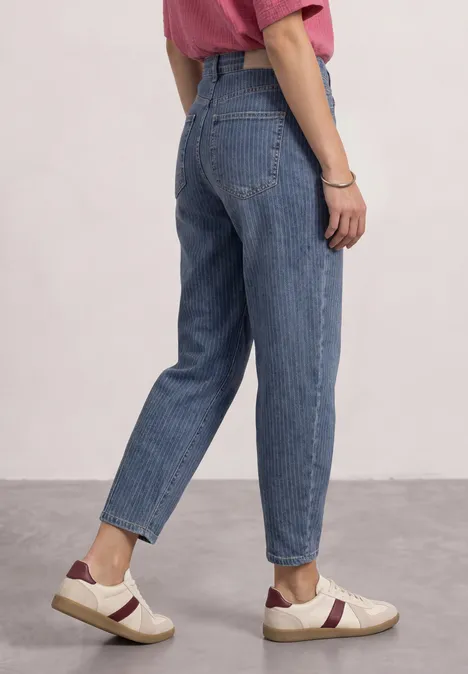 Seitliche Ansicht einer Person in blauen Jeans und weißen Sneakern mit bordeauxfarbenem Streifen.
