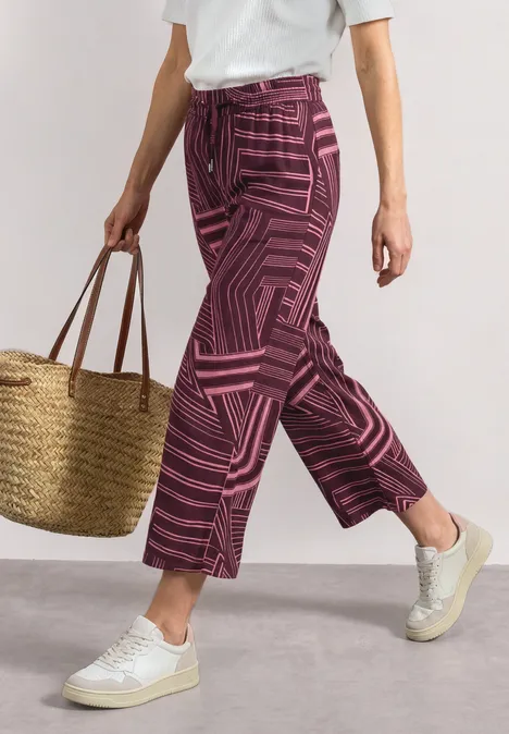 Culotte taille haute à motifs blush berry Frau trägt weißes T-Shirt, gemusterte pinke Culotte, weiße Sneaker und Korbtasche.
