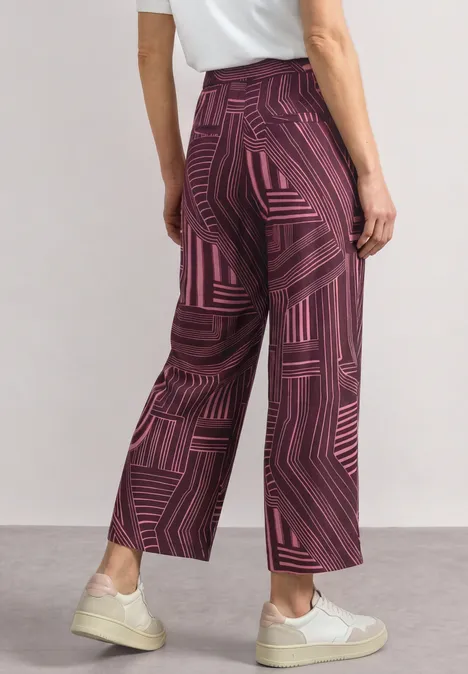 Culotte taille haute à motifs blush berry Frau trägt burgunderrote, weit geschnittene Hosen mit geometrischem Muster, kombiniert mit weißem Shirt und Sneakers.