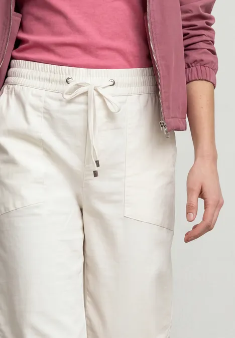 Eine Person trägt eine rosa Jacke, ein pinkes Top und helle, locker sitzende Hose mit Kordelzug.