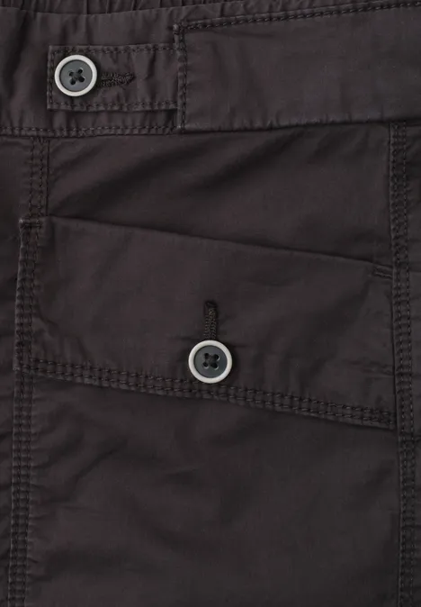 Detailaufnahme eines dunklen Kleidungsstücks mit zwei Knöpfen und einer aufgesetzten Tasche.