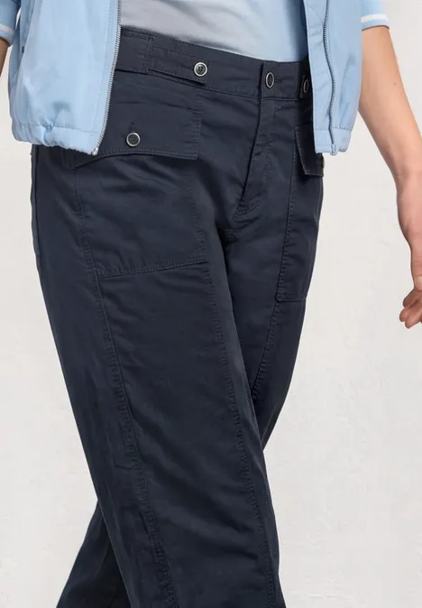 Nahaufnahme von dunkelblauen Cargo-Hosen mit aufgesetzten Taschen und hellblauem Oberteil.