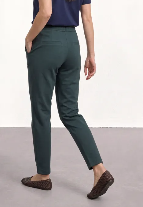 Frau von hinten trägt dunkelgrüne, schmal geschnittene Hose und braune Loafers.
