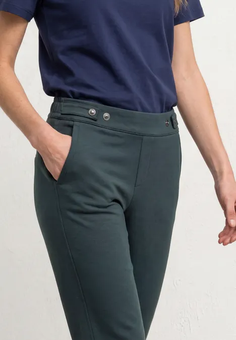 Frau trägt dunkelgrüne, taillierte Hose mit Knopfverschluss und Seitentaschen, dazu ein marineblaues T-Shirt.