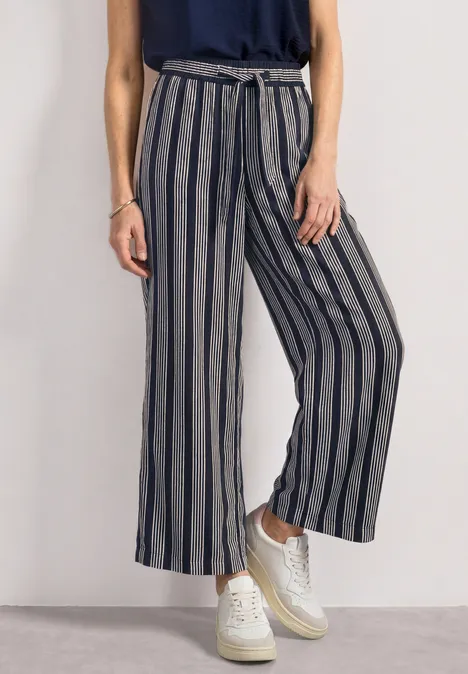 Pantalon ample gris à rayures noires, taille haute avec ceinture nouée, porté avec baskets blanches.