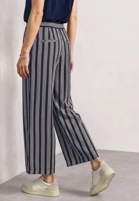 Vue arrière latérale d'une personne portant un pantalon ample à rayures gris-bleu et des baskets claires.