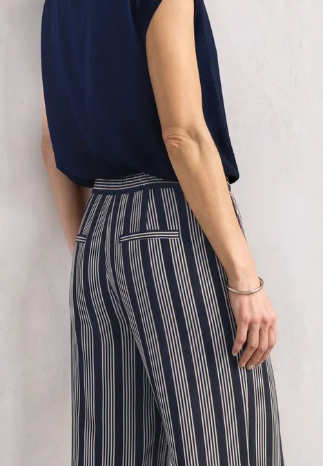 Femme en top bleu marine et pantalon gris-bleu à rayures verticales, vue latérale.