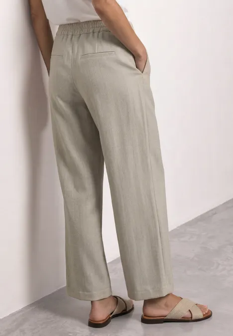 High Waist Straight Leg Hose im Casual Fit dark creamed sand Person von hinten in beigen, weiten Hosen und flachen Sandalen vor hellem Hintergrund