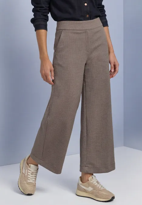High Waist Culotte im Casual Fit black coffee Model trägt weite, knöchellange, beige Stoffhose mit Seitennahttaschen und beigefarbenen Sneakers.