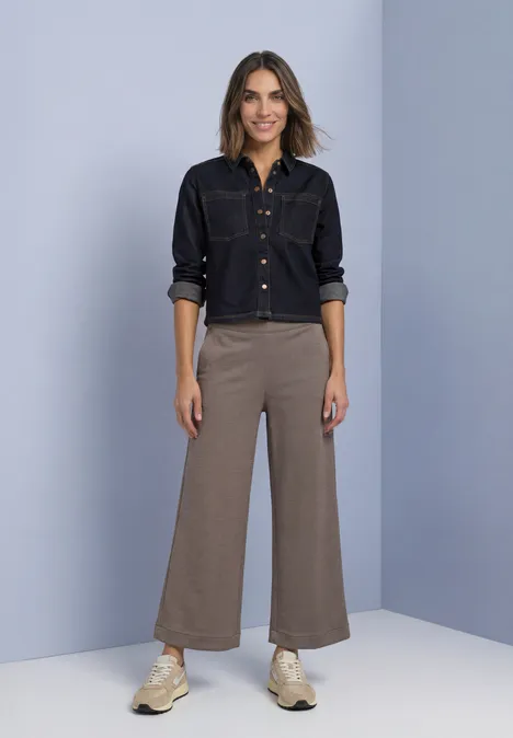 High Waist Culotte im Casual Fit black coffee Frau in schwarzem Jeanshemd, weiten, knöchellangen Hosen und Sneakers vor neutralem Hintergrund.