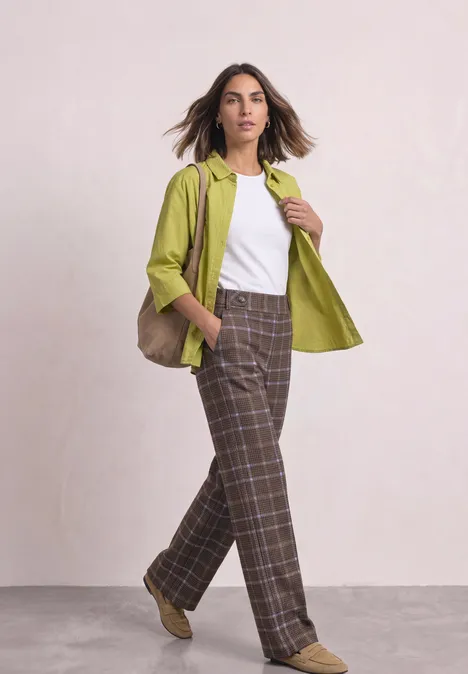 Wide Leg Velorus Hose im Casual Fit silk brown Frau im weißen Top, grüner Jacke und karierten Hosen posiert vor neutralem Hintergrund.