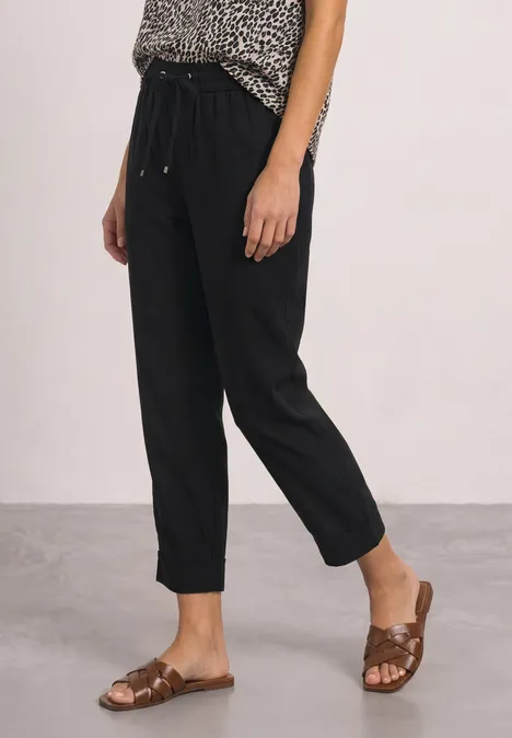 Frau trägt schwarze, knöchellange Hose mit lockerer Passform und braune, flache Sandalen.