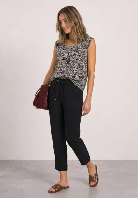 Frau trägt gemustertes ärmelloses Top, schwarze Hose, braune Sandalen und rote Schultertasche.