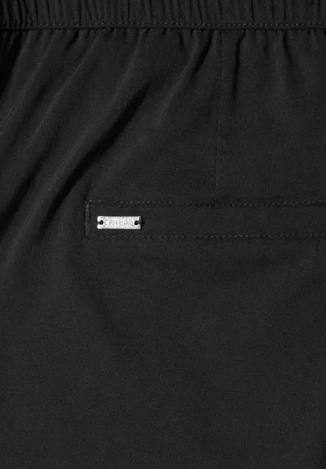 Nahaufnahme einer schwarzen Hose mit Gummibund und einer kleinen Metallplakette an der Tasche.