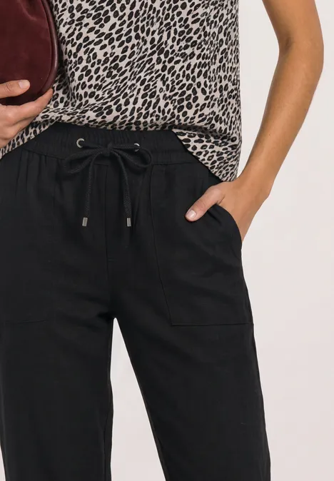 Frau trägt schwarze Hose mit Tunnelzug, Leoparden-Top und eine bordeauxrote Clutch.