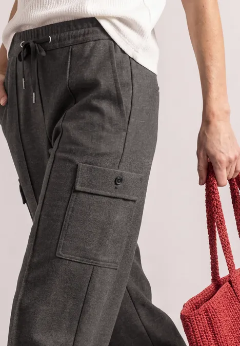 Donkergrijze cargobroek met zijzakken en een rode gebreide tas in de hand.