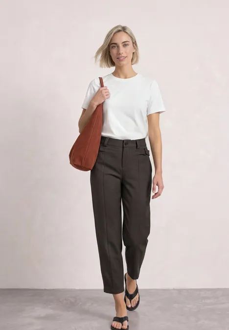 High Waist Barrel Leg Hose im Casual Fit black coffee Frau im weißen T-Shirt, dunkler Hose und Flip-Flops mit brauner Schultertasche.