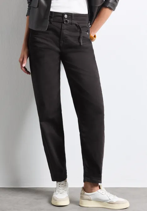 High Waist Barrel Leg Jeans im Loose Fit Brown Washed Frau trägt schwarze High-Waist-Jeans, weiße Sneaker, weiße Socken, weißes T-Shirt und schwarze Jacke.
