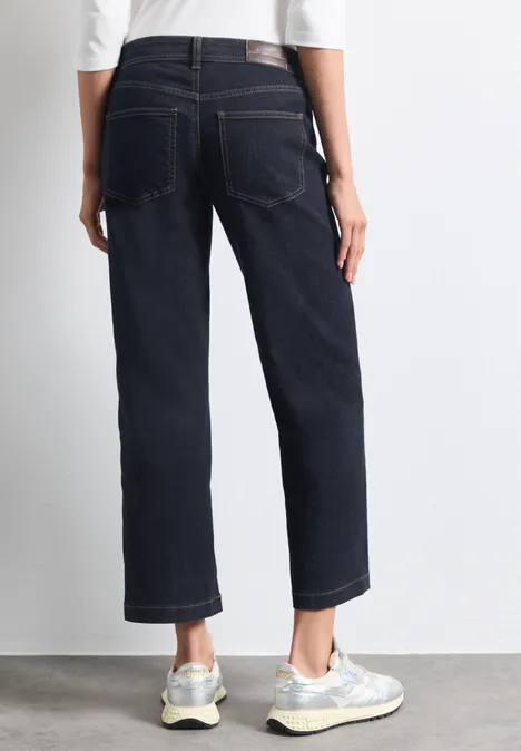 Persoon van achteren in donkere, rechte jeans en witte sneakers.