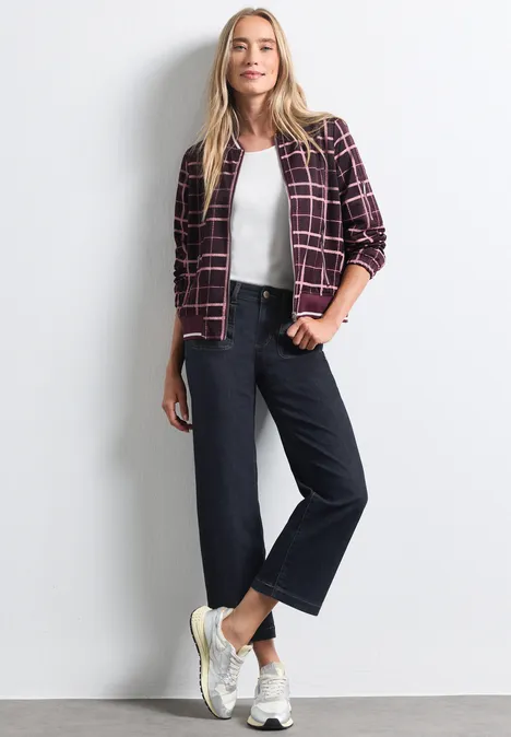Vrouw in een casual outfit: ruitjasje, wit topje, wijde jeans en witte sneakers.