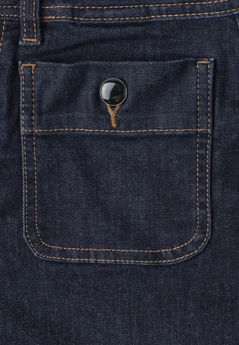 Close-up van een donkerblauwe spijkerbroek met oranje stiksels en knoop op een zak.