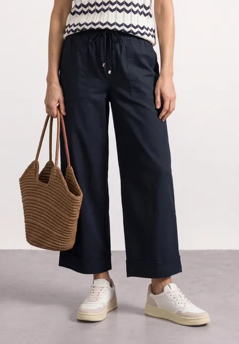 Pantalon Straight Leg et décontracté, avec revers darkest blue Personne portant un pantalon large bleu nuit, un top rayé, des baskets blanches et un sac tissé marron.