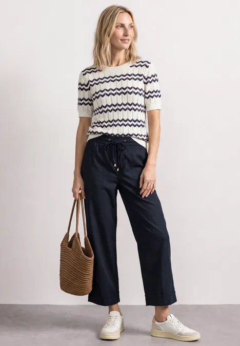 Pantalon Straight Leg et décontracté, avec revers darkest blue Une femme porte un haut rayé, un pantalon large, des baskets blanches et tient un sac tressé.