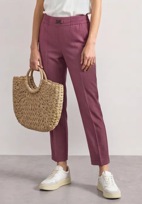 Slim Leg Hose mit Schnallendetail dark clouded blush Person trägt rosafarbene Hose, weiße Sneaker und eine geflochtene Strohtasche in der Hand.