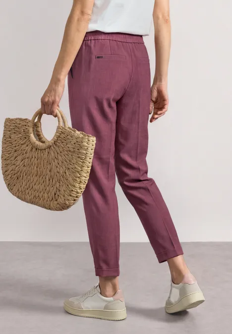 Slim Leg Hose mit Schnallendetail dark clouded blush Frau trägt weinrote Anzughose, weiße Sneaker und hält einen geflochtenen Strohkorb.