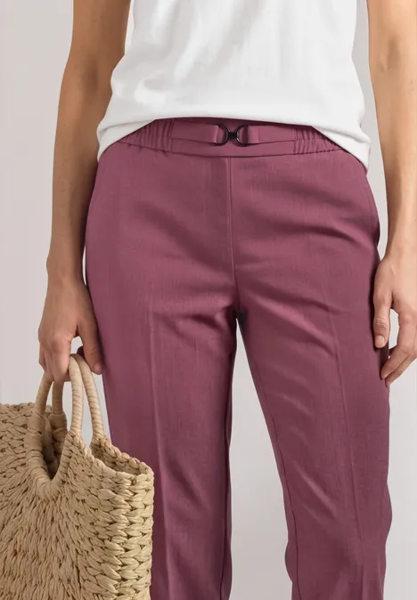 Slim Leg Hose mit Schnallendetail dark clouded blush Eine Person trägt eine weiße Bluse, plumfarbene Hose und hält eine Strohtasche.