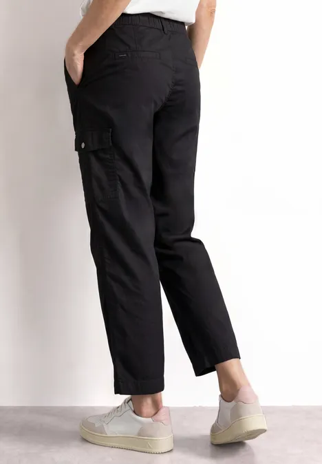 Pantalon cargo noir longueur chevilles, coupe droite, poches latérales, porté avec des baskets blanches.