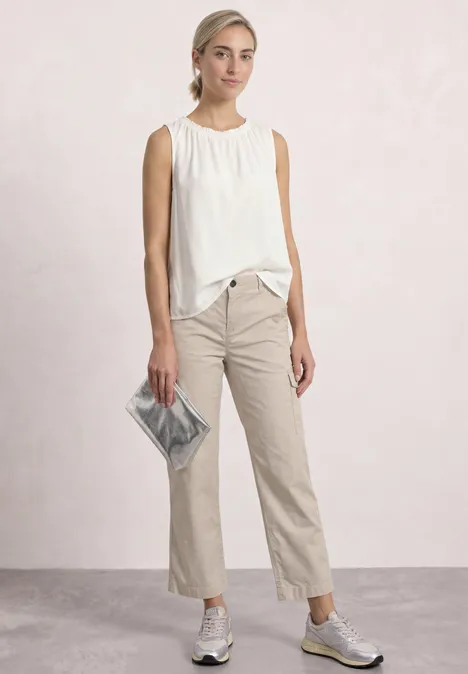 Straight Leg Hose im Cargo-Look clay sand Frau in weißer Bluse, beigen Hosen, Sneakers und silberner Clutch vor hellem Hintergrund.