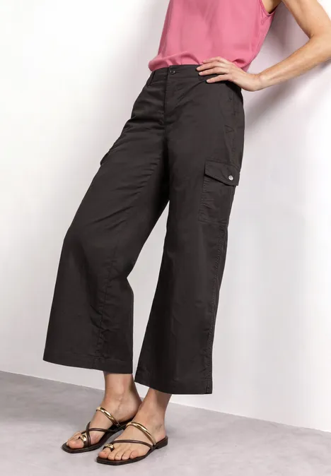 Pantalon cargo noir ample, longueur cheville avec poches latérales, porté avec sandales fines noires et top rose.